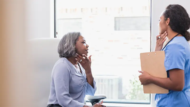 A nurse seeing to a patient who is touching their neck.