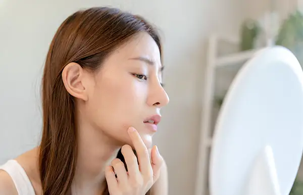 A woman touching a pimple while looking in a mirror