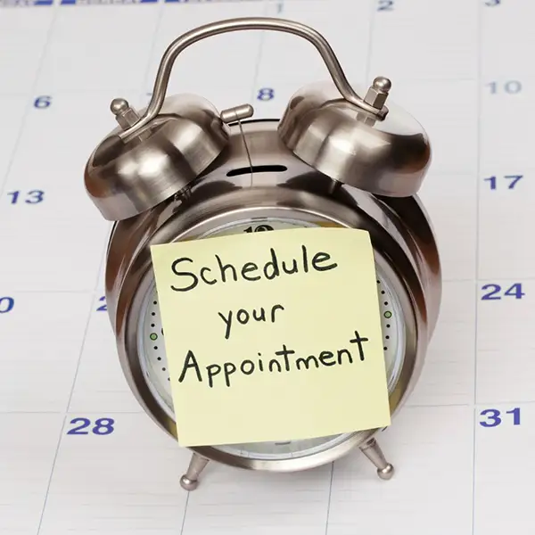 A clock, sitting atop a calendar, with a sticky note that reads 'Schedule your Appointment'