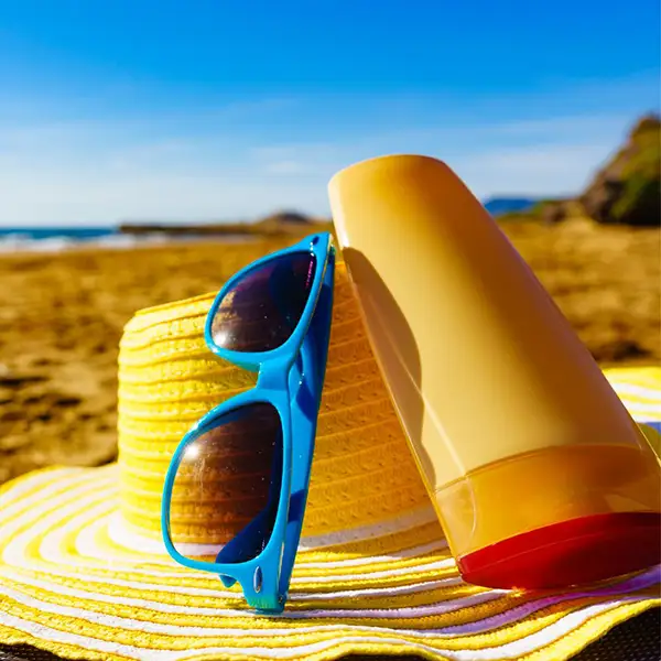 A hat, sunglasses, and sun screen on a beach.
